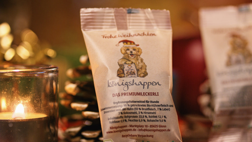 Königshappen Weihnachtsedition – 10-g-Päckchen mit Nikolausmütze-Hund vor Kerze und Tannenzapfen