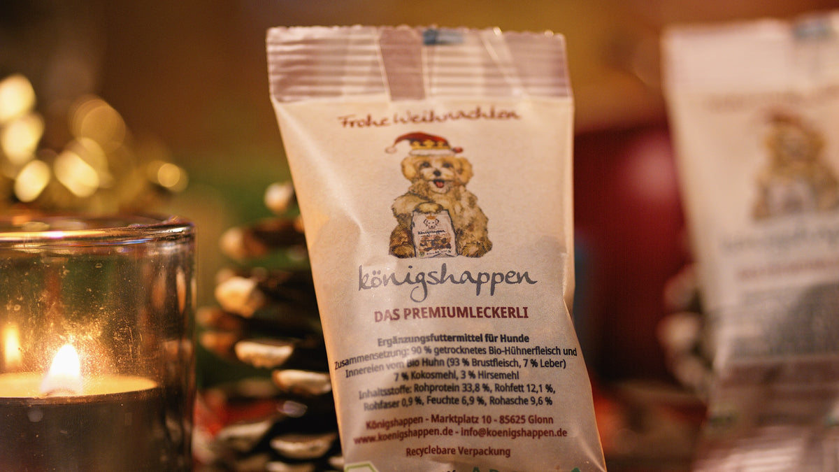 Königshappen Weihnachtsedition – 10-g-Päckchen mit Nikolausmütze-Hund vor Kerze und Tannenzapfen